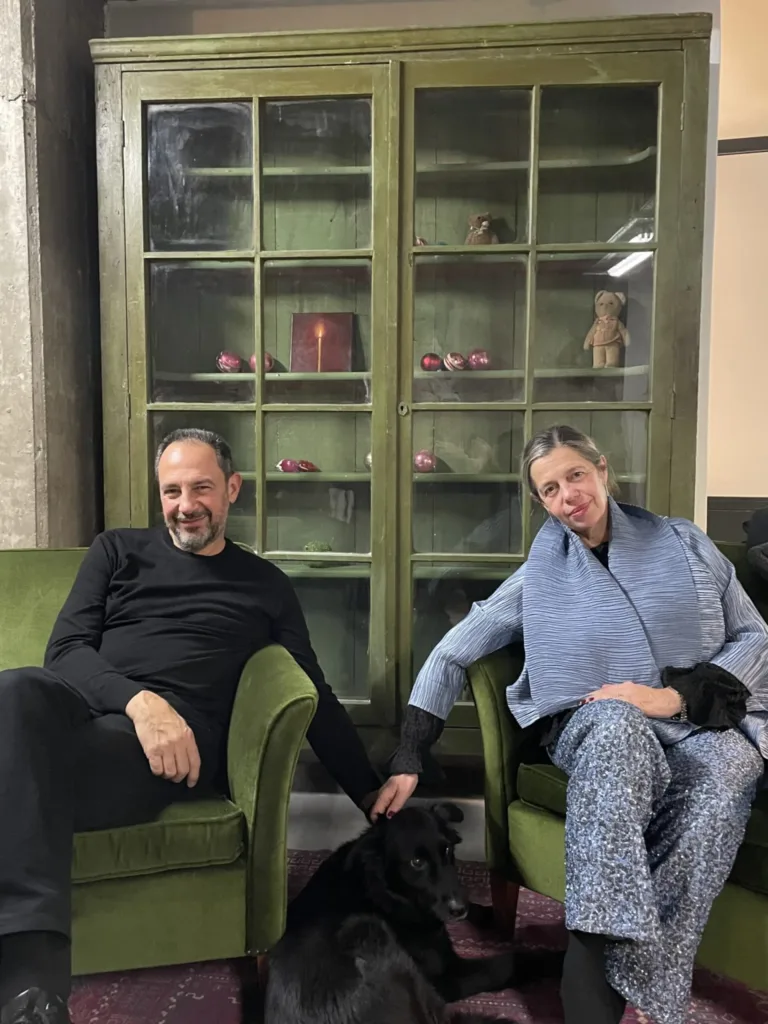 Hosts seated in green velvet armchairs with a black dog, before a green glass cabinet at A Place ApArt