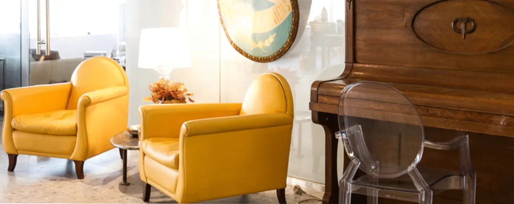 Apart Suite in Athens: two mustard-yellow armchairs beside a vintage wooden piano and a clear acrylic chair
